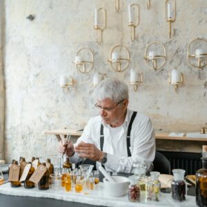 Senior perfumer blends fragrant ingredients in stylish indoor setting.