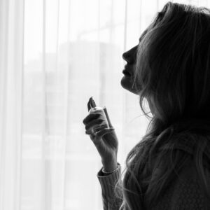 Silhouette of a woman holding and spraying perfume by a window curtain.